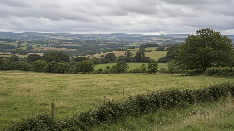 English patchwork farmland with a ploughed field, hedgerows, a five-bar gate and a distant church tower